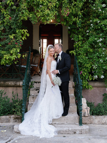 Newlyweds standing together beneath lush greenery during their Pyrgos Ralli wedding portraits