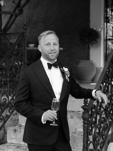 Black and white groom portrait holding a champagne glass at Pyrgos Ralli