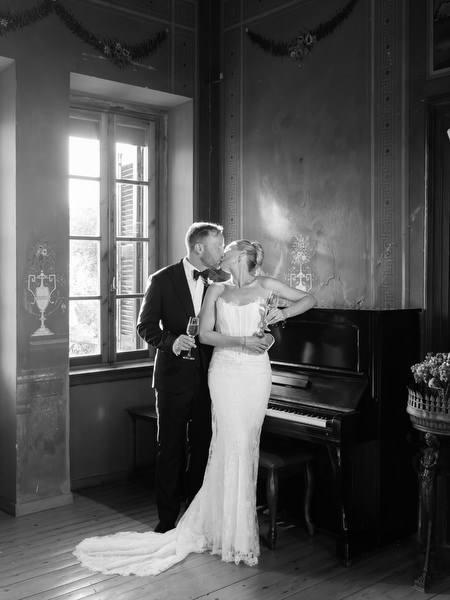 Black and white wedding portrait of the couple beside a piano in the historic venue