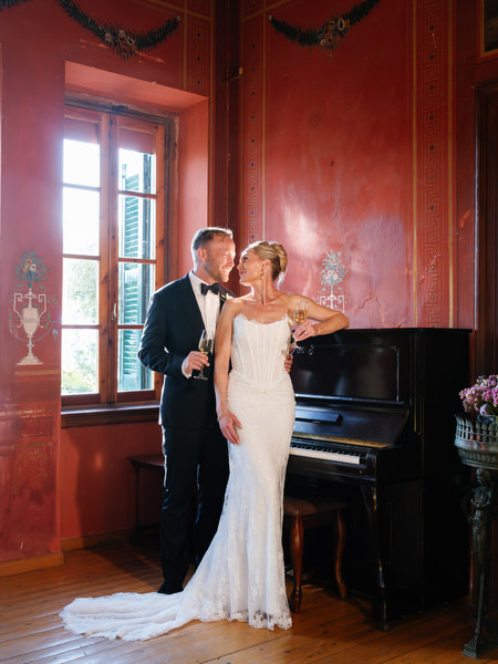 Bride and groom posing beside a piano during elegant indoor wedding portraits