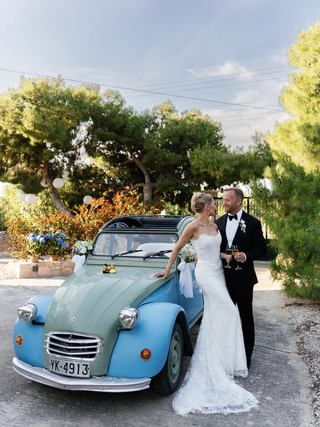 Bride and groom posing beside a vintage blue car during their Aegina wedding portraits