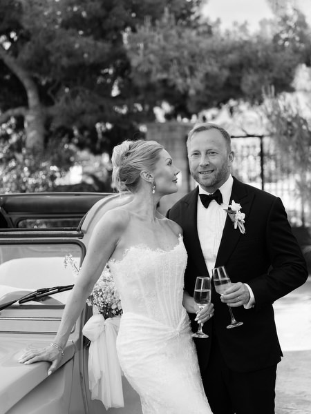 Black and white portrait of the newlyweds beside a classic car at Pyrgos Ralli