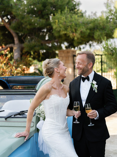 Bride and groom smiling together beside a vintage car during their Pyrgos Ralli wedding portraits
