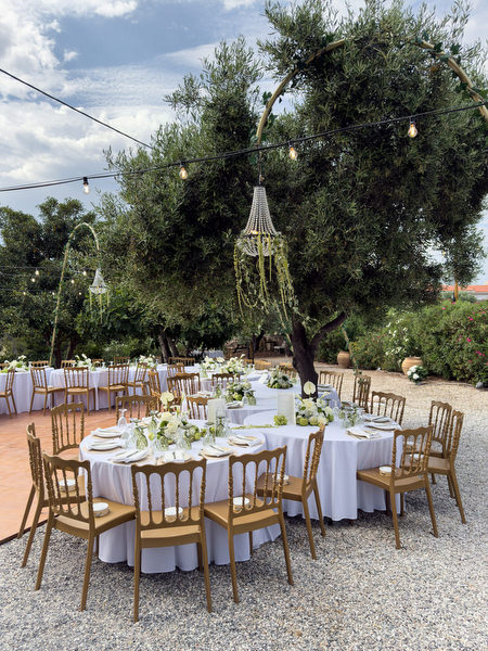 Al fresco wedding dinner setup with wooden chairs and white florals in Aegina