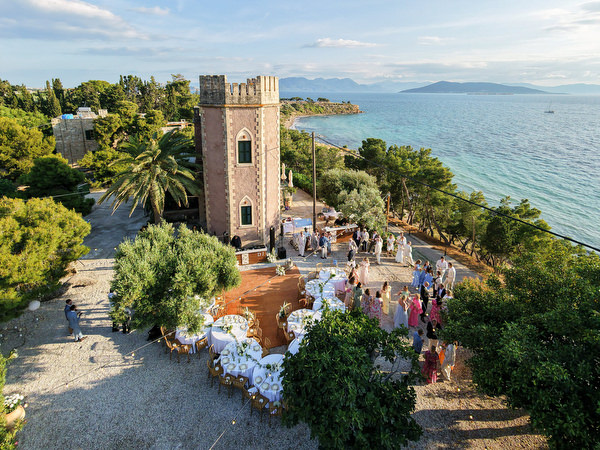 Wide view of Pyrgos Ralli, outdoor reception tables and the Aegina coastline