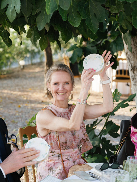 Wedding guest smiling and holding a handheld fan during the outdoor reception in Aegina