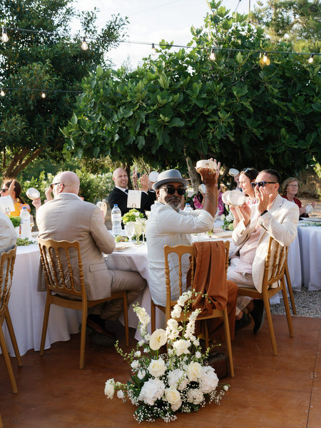 Guests seated at long dinner tables beneath greenery at a Pyrgos Ralli wedding