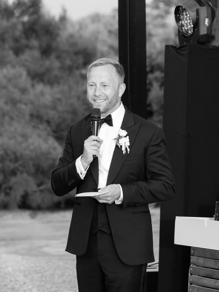 Black and white portrait of the groom giving a speech during the evening reception