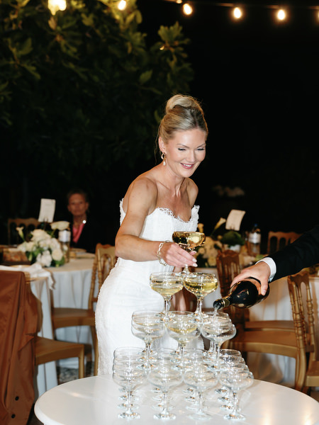 Bride pouring champagne into a tower of glasses during the Pyrgos Ralli celebration