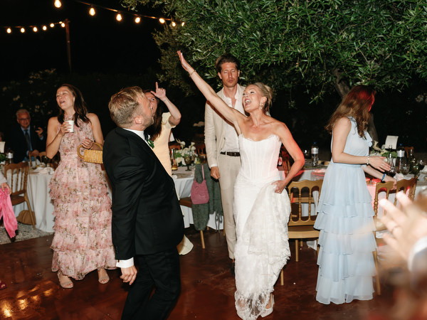 Bride and groom dancing with guests beneath string lights at their Aegina wedding