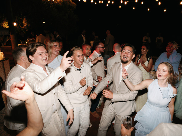 Wedding guests dancing enthusiastically beneath string lights at the Pyrgos Ralli party