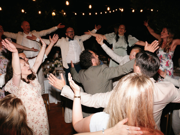 Wedding guests raising their arms and dancing beneath string lights at Pyrgos Ralli