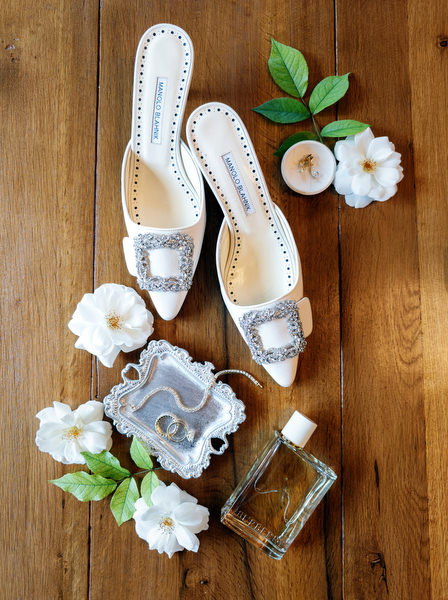 Bridal shoes and wedding accessories styled with white flowers on a wooden table