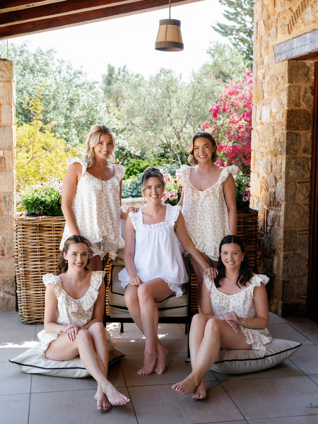 Bride and bridesmaids posing together beneath Mediterranean greenery