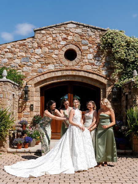 Bride and bridesmaids posing with the lace gown spread across the courtyard