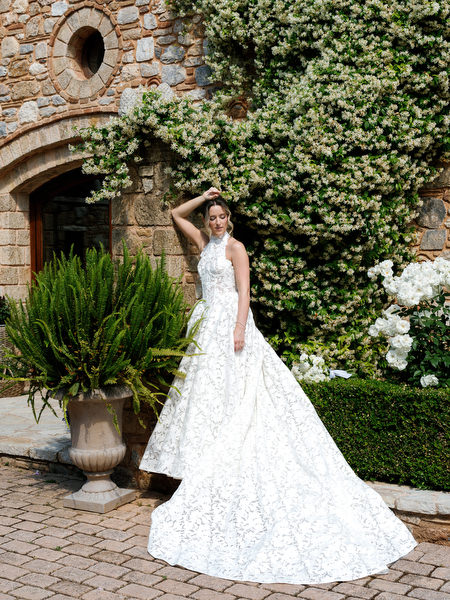 Bride posing alone beside stone walls and Mediterranean greenery at Pyrgos Petreza