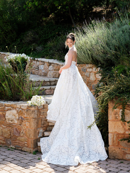 Full-length bridal portrait along a stone path surrounded by olive trees and greenery