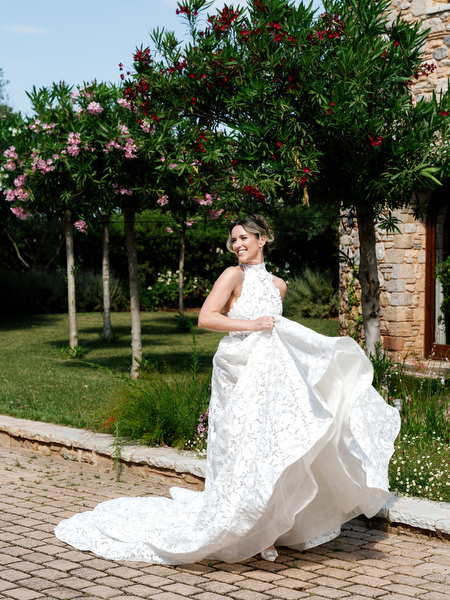 Bride posing with her lace wedding gown beneath flowering trees at Pyrgos Petreza