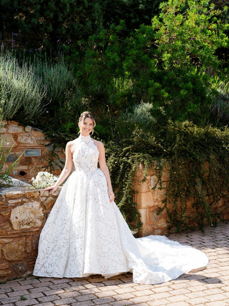 Bride standing beside a stone wall and Mediterranean greenery before the ceremony