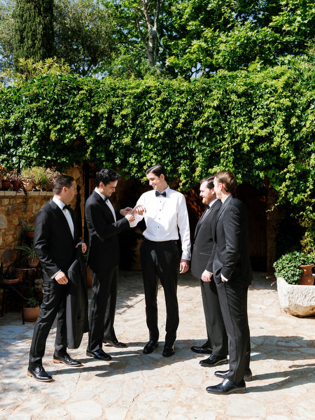 Groom and groomsmen gathering beneath lush greenery before the wedding ceremony