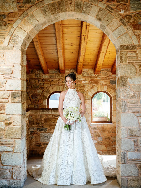 Bride standing beneath the historic stone arch in her lace wedding gown