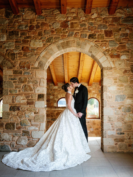 Newlyweds posing beneath the rustic stone arch inside the Athens wedding venue
