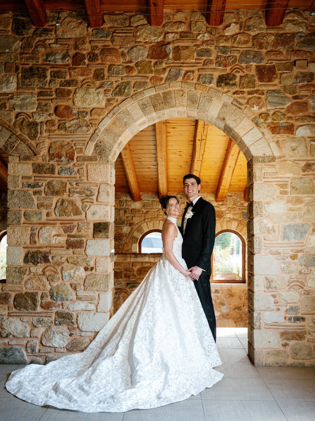 Bride and groom standing together beneath an illuminated stone arch