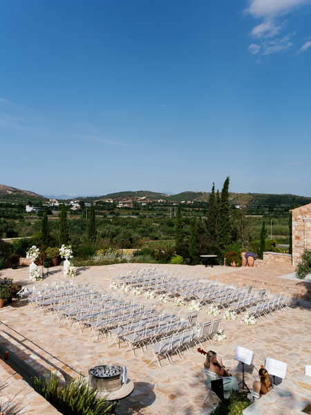Wide view of the outdoor ceremony seating at Pyrgos Petreza beneath a clear blue sky