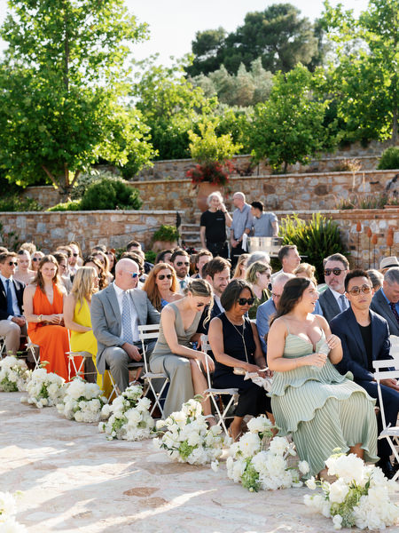 Wide view of guests seated beside white floral arrangements during the outdoor ceremony