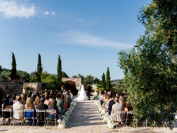 Wide view of the flower-lined aisle and guests beneath the Greek summer sky