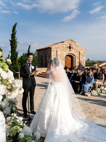 Bride seen from behind walking toward the groom in her lace gown and veil