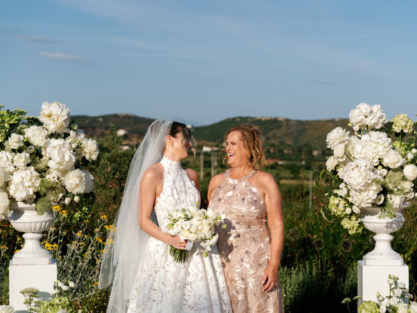Bride sharing a portrait with a bridesmaid beside the white floral ceremony backdrop