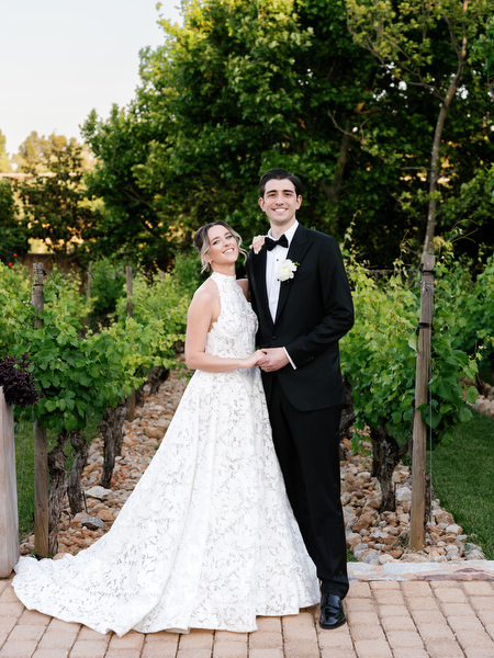 Newlyweds standing together along a stone path in the gardens of Pyrgos Petreza