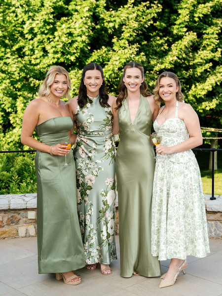 Four wedding guests in elegant green dresses posing together outdoors