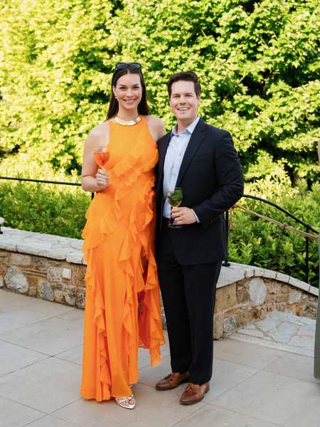 Wedding guest in an orange dress posing with a man in a dark suit