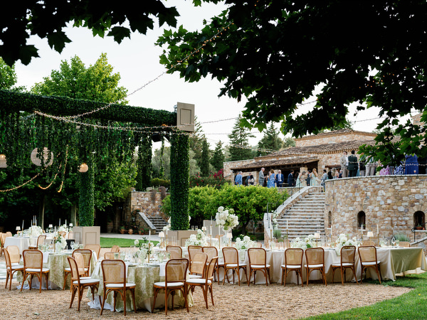 Outdoor wedding reception tables arranged beneath a canopy of hanging greenery