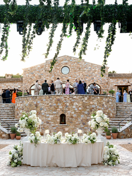Sweetheart table decorated with white florals beneath cascading greenery