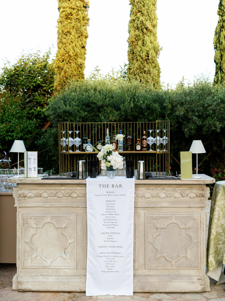 Wedding coctail bar displayed on a decorative stone table beneath tall cypress trees