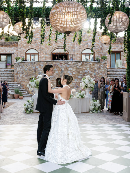 Bride and groom beginning their first dance beneath woven lights and hanging greenery