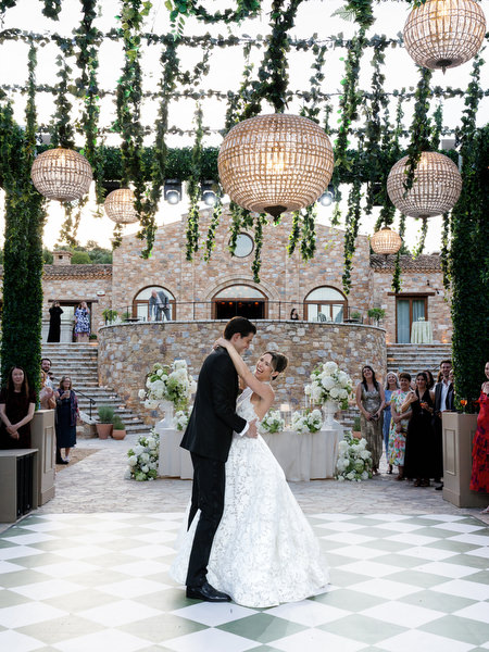 Newlyweds sharing their first dance beneath hanging greenery and woven lanterns