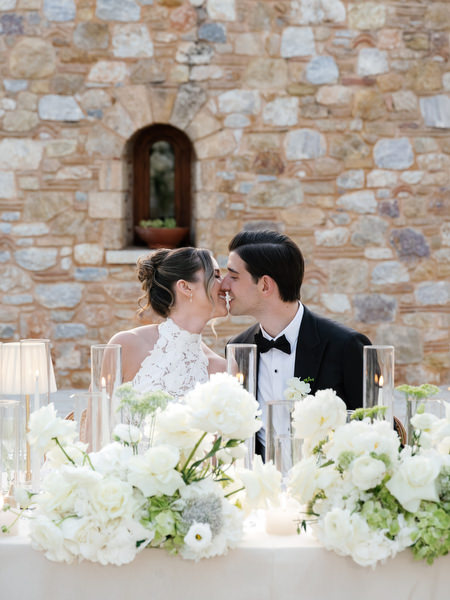 Bride and groom smiling together at their flower-filled sweetheart table