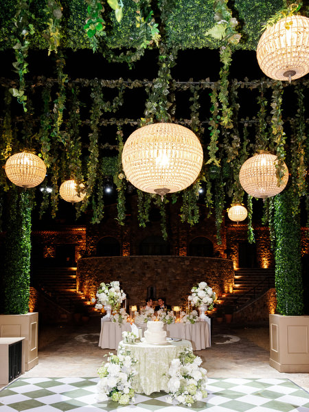 Sweetheart table glowing beneath woven lanterns and cascading greenery at night