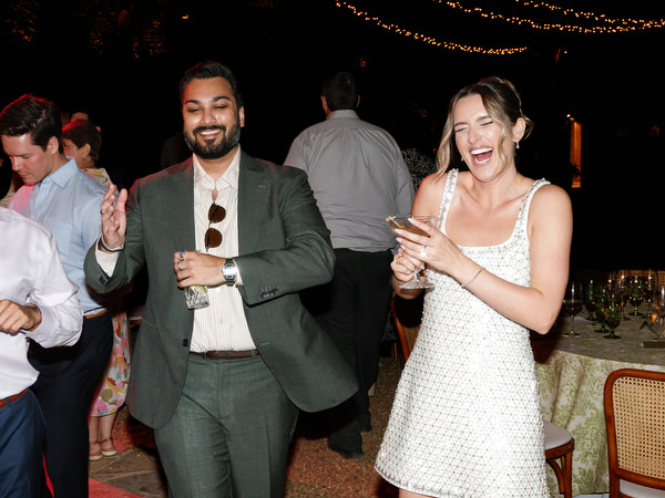 Wedding guests laughing and dancing beneath warm string lights near Athens