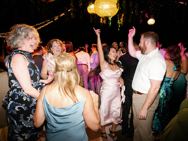Crowded wedding dance floor filled with guests dancing under string lights